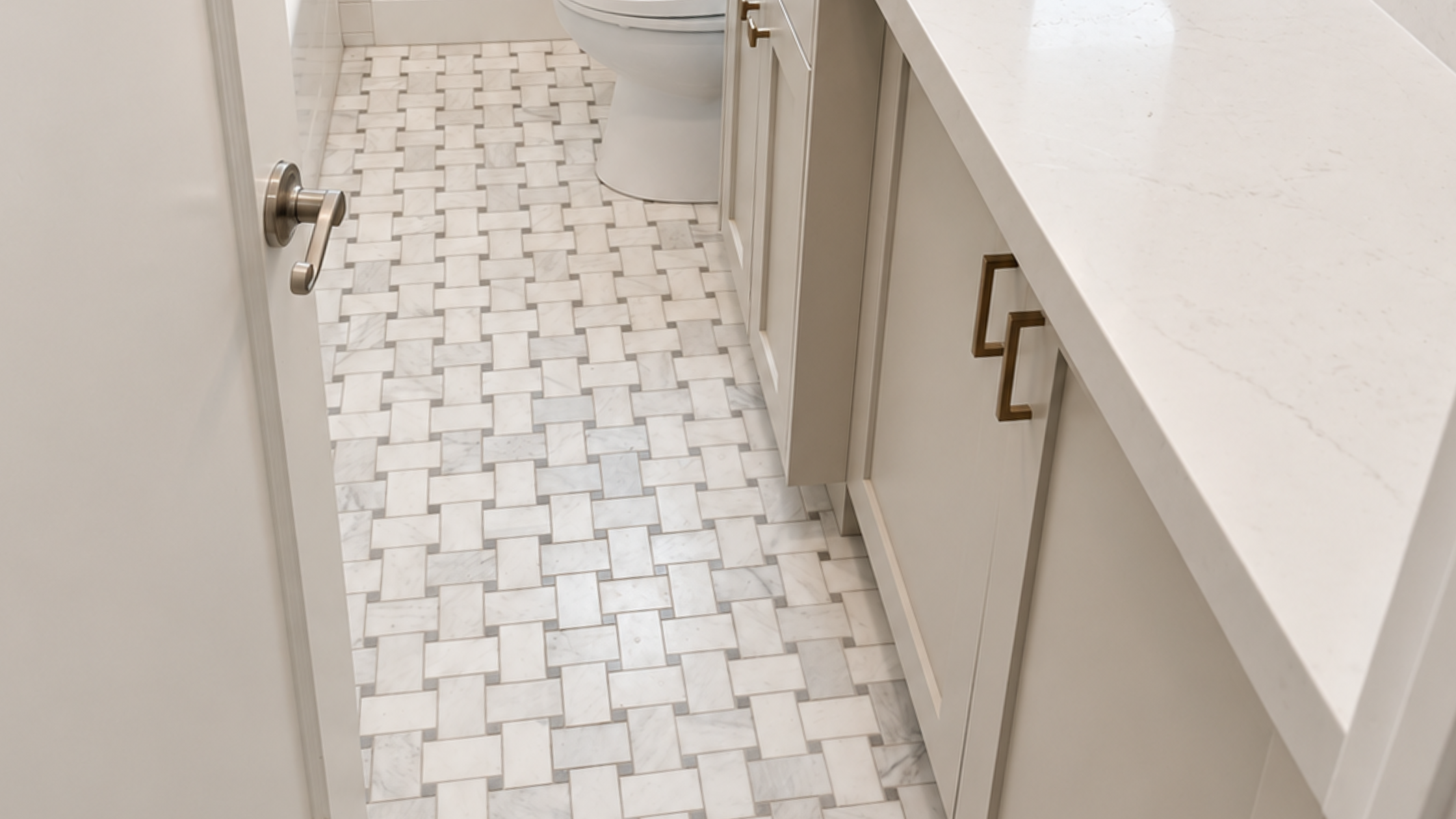 Remodeled bathroom with woven marble tile flooring, light cabinetry, quartz countertop, and brass hardware.