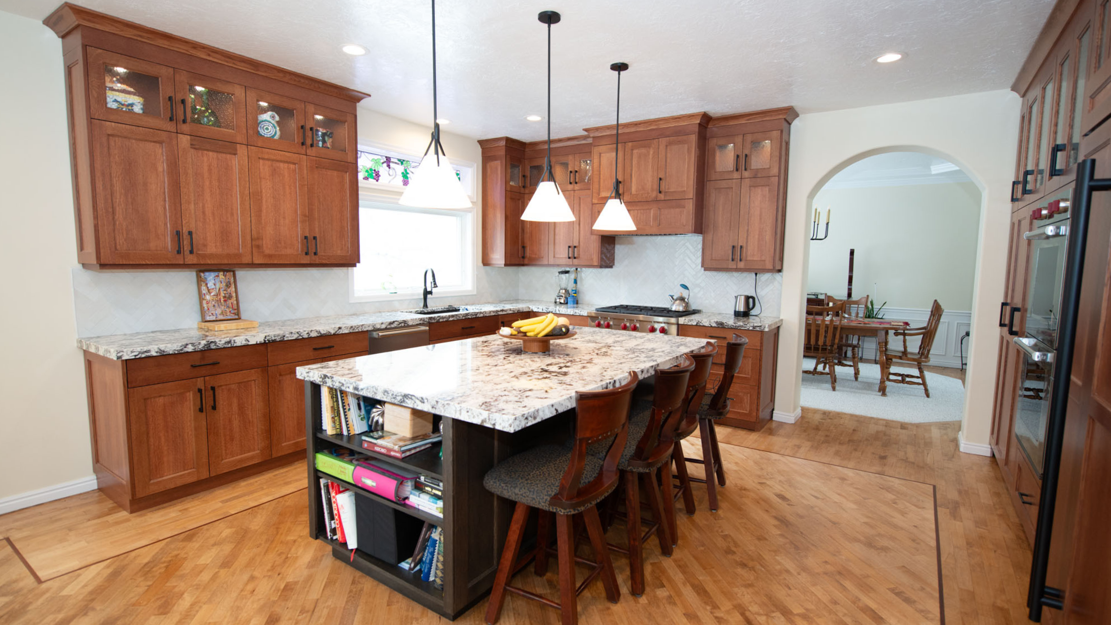 Updated Utah kitchen with warm wood cabinetry, a large stone island, pendant lighting, and an open connection to the dining room.