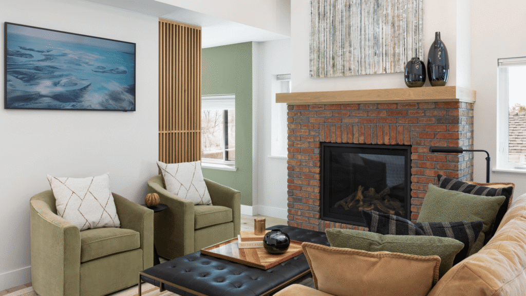 Remodeled living room featuring a restored brick fireplace, green chairs, white oak accents, and modern furnishings.